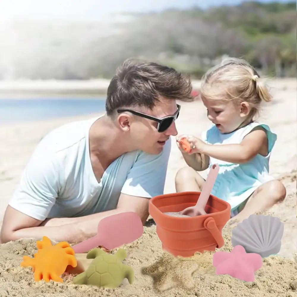Child using silicone spade and rake with colourful sand moulds on the beach