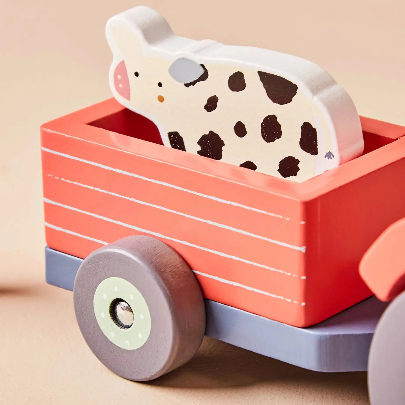 Wooden toy cow in a red wagon with a beige background