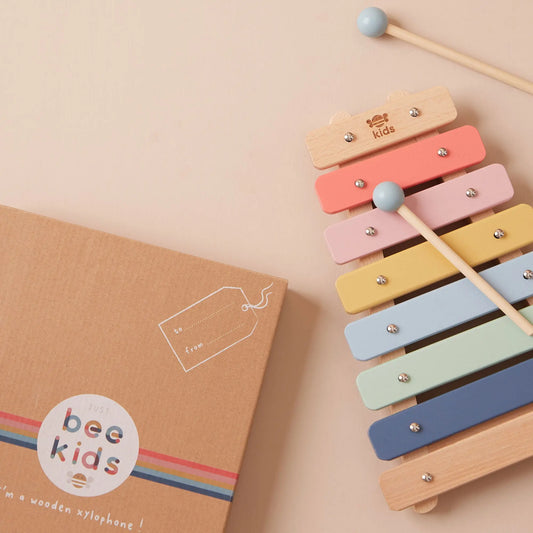 Colourful wooden xylophone with 'just bee kids' branding next to its packaging on a beige background