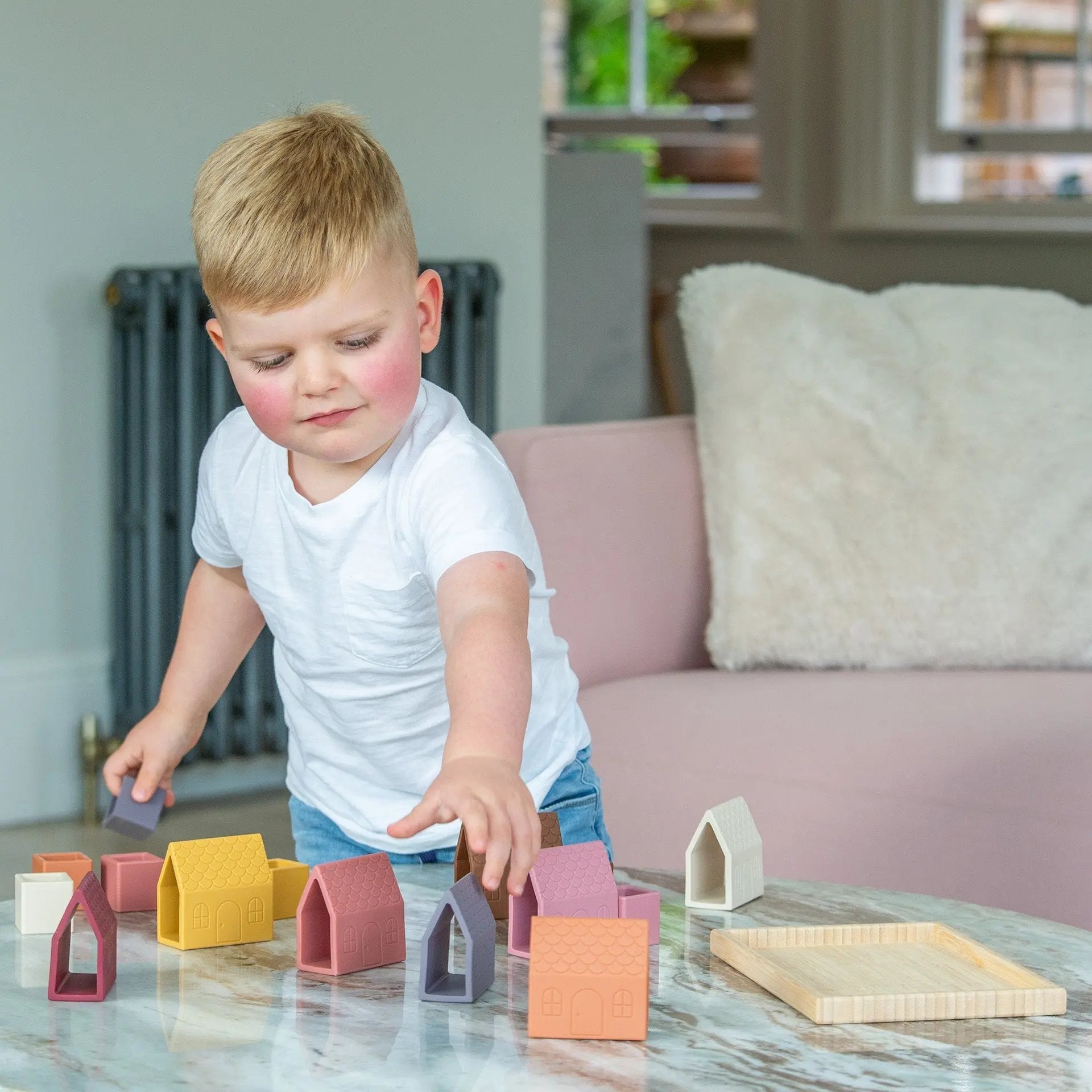 Child playing with colourful silicone blocks on a marble surface in a living room.