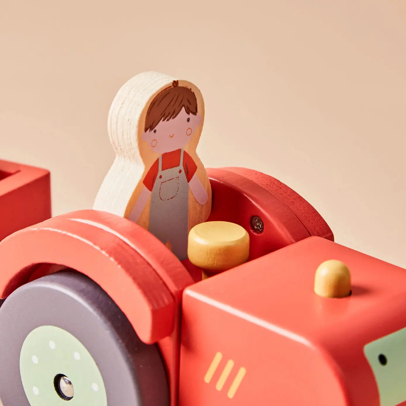 Wooden toy farmer figure sitting inside a red toy tractor on a beige background