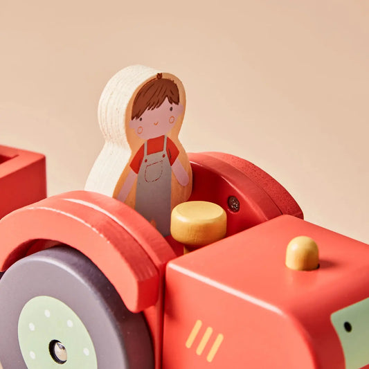 Wooden toy farmer figure sitting inside a red toy tractor on a beige background