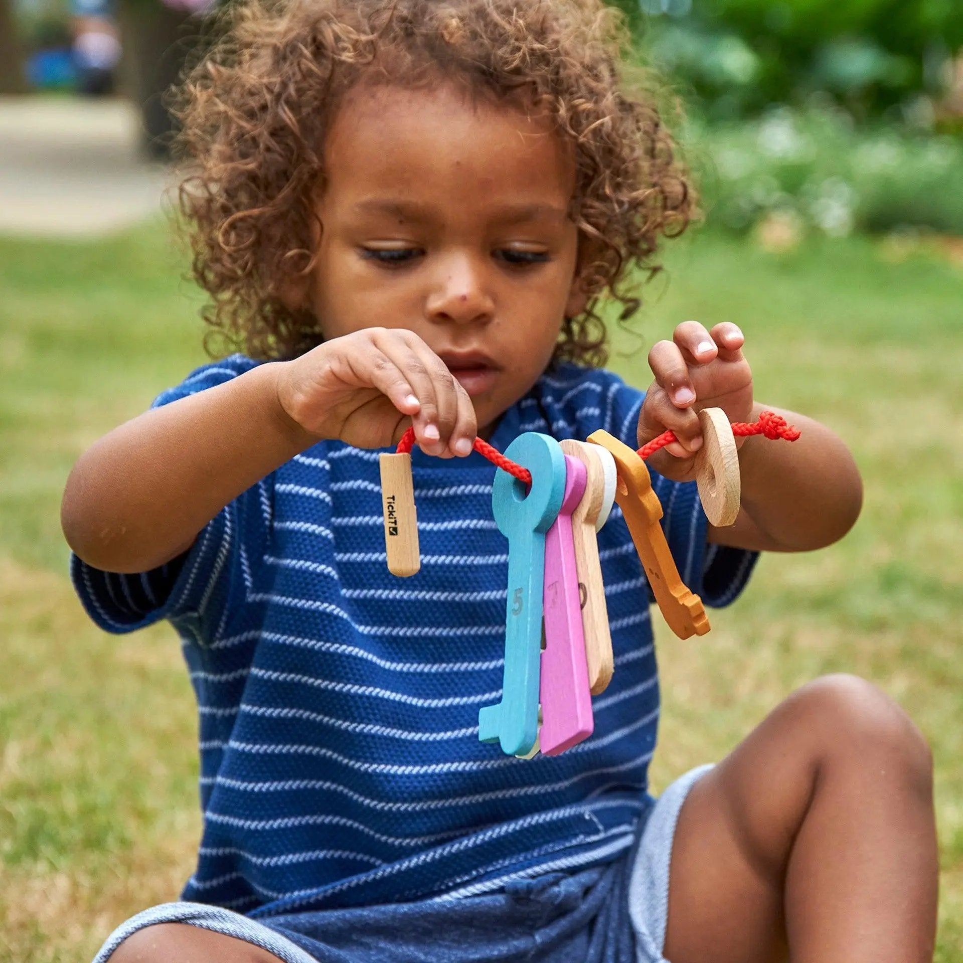 Child playing with colourful keys outdoors on grass