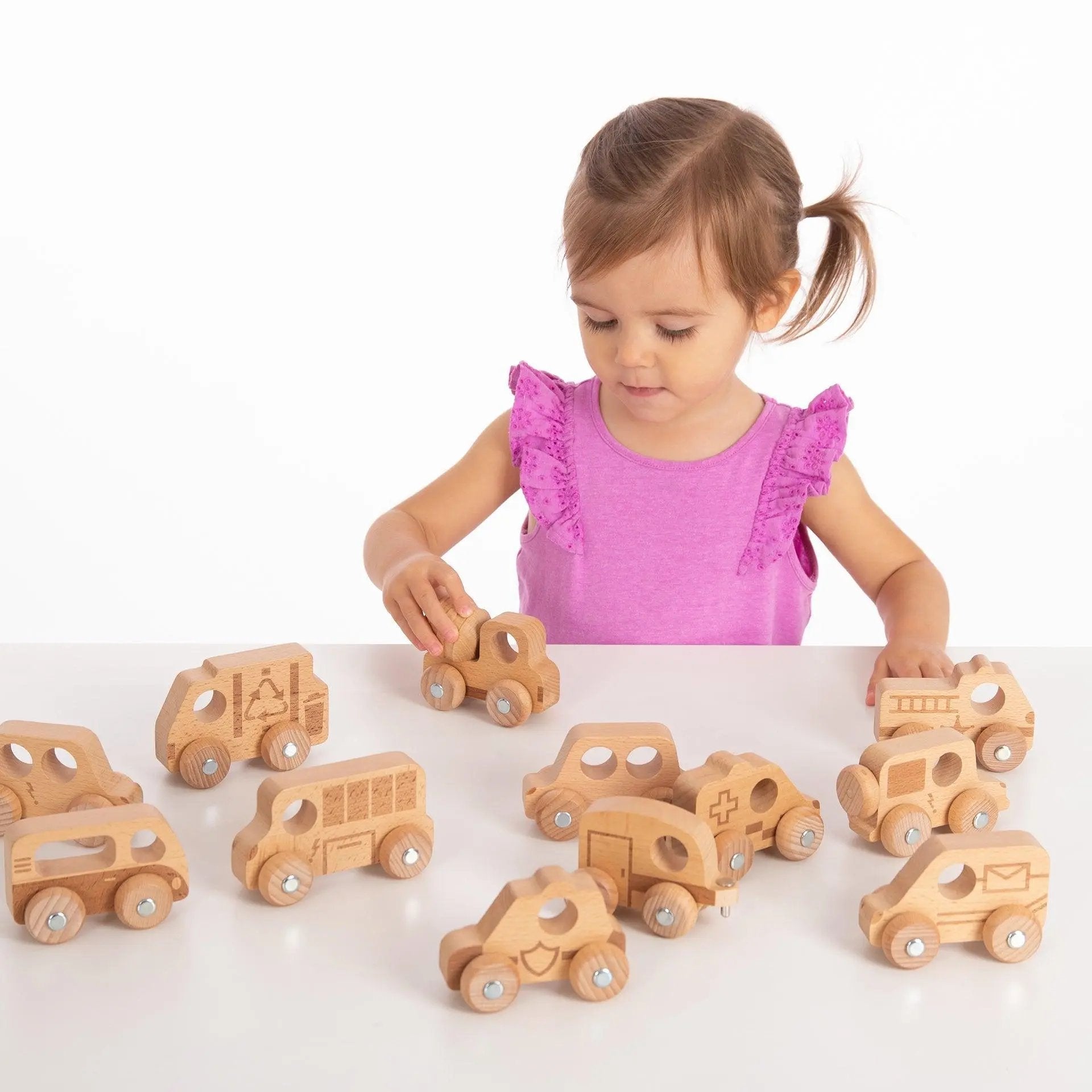 Child playing with wooden toy cars on a white surface