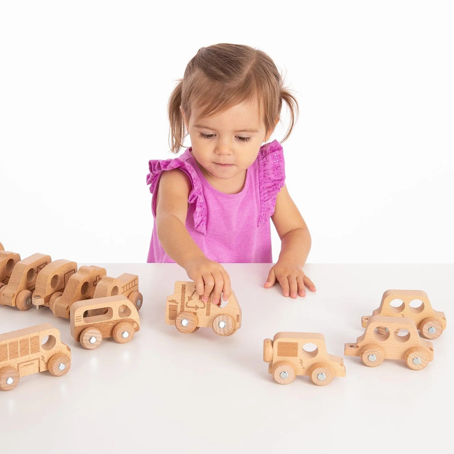 Child playing with wooden toy cars on a white surface