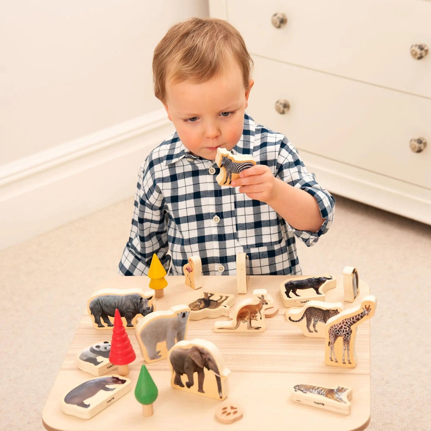 Child playing with wooden animal toys on a light-coloured floor.