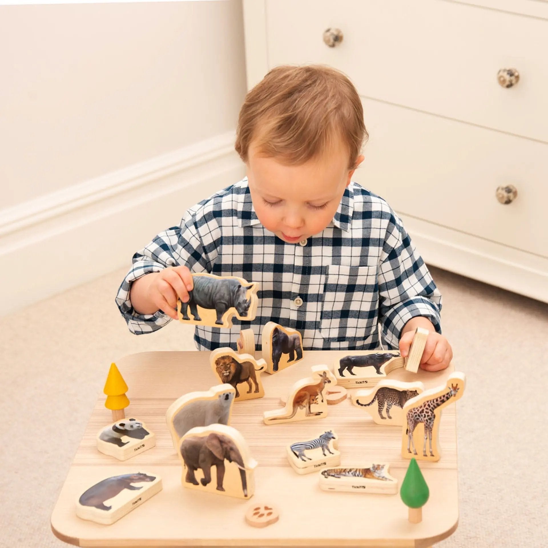 Child playing with wooden animal puzzle on a light-coloured floor.