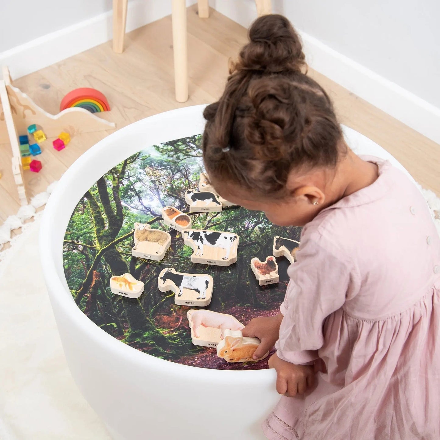 Child playing with animal toys on a round table with a nature-themed surface