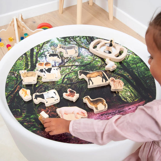 Child playing with animal figurines on a round table with a forest design