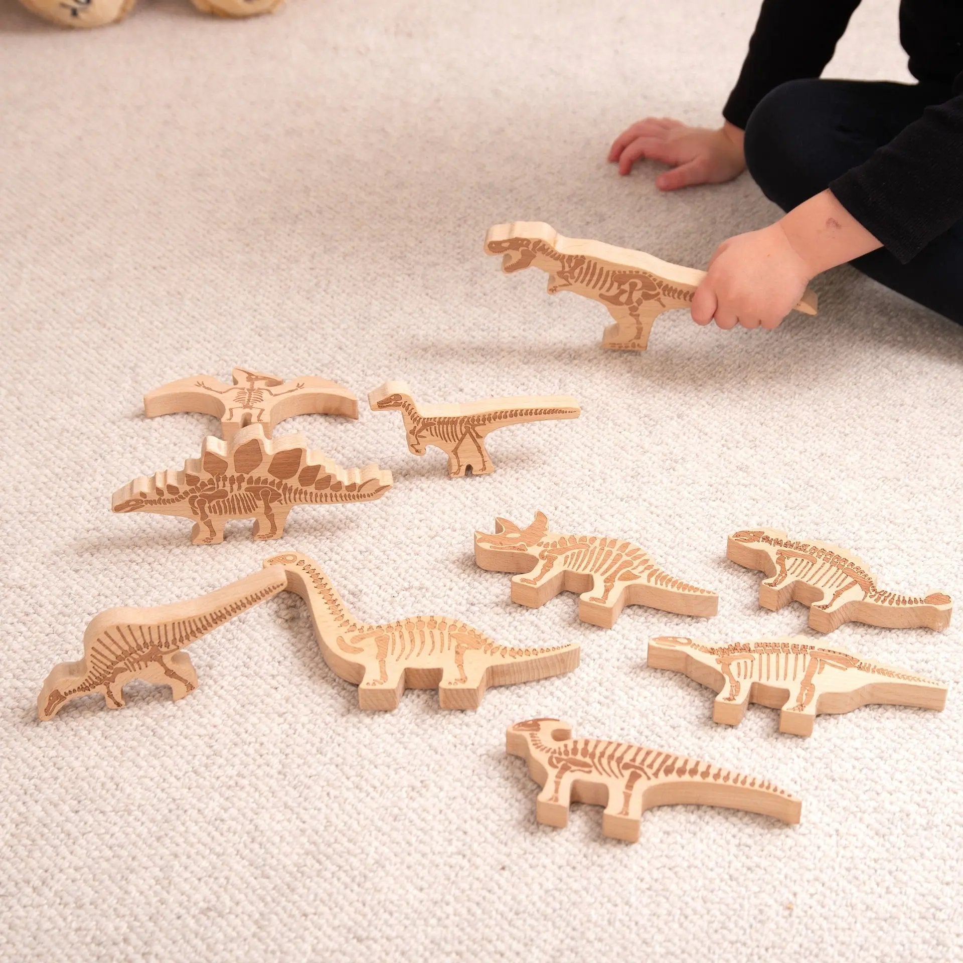 Wooden dinosaur fossils on a carpeted floor with a child's hand reaching for one.