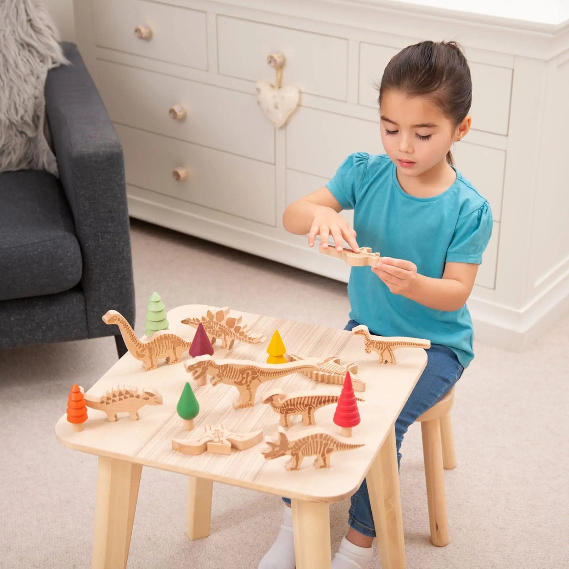 Child playing with wooden dinosaur toys on a table in a room.