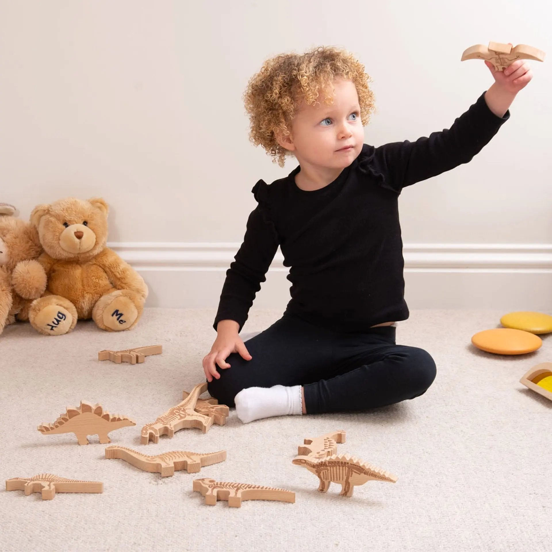 Child playing with wooden dinosaur toys on a carpeted floor.