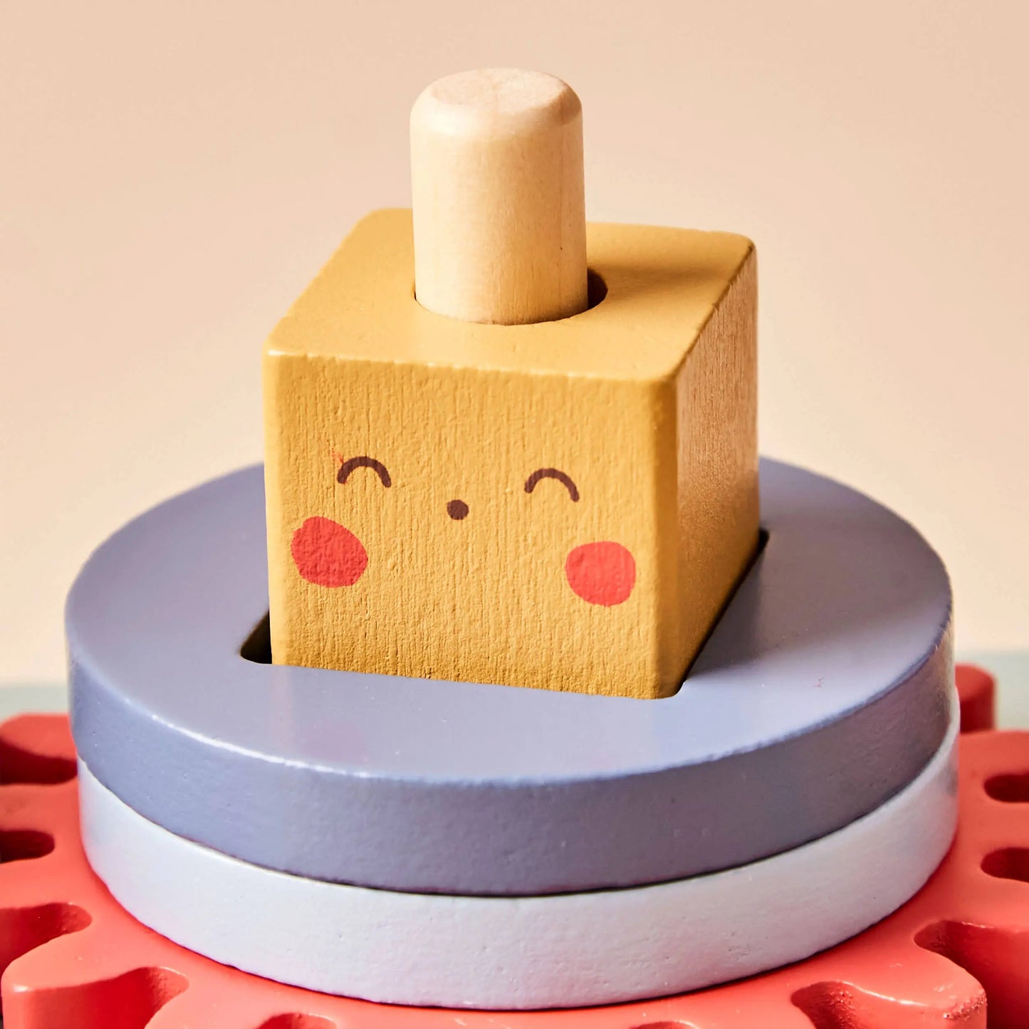 Wooden toy with a smiley face block on top of stacked rings against a beige background