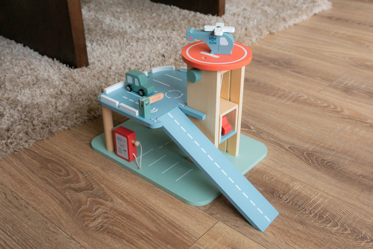 Toy set with a helicopter, cars, and a ramp on a wooden floor.