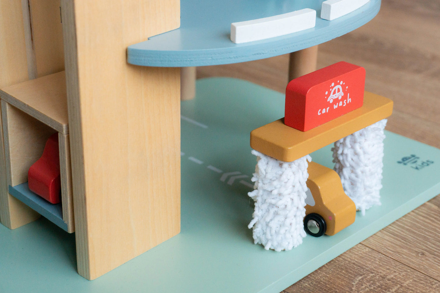 Toy car wash set with wooden structure and colourful elements on a wooden floor.