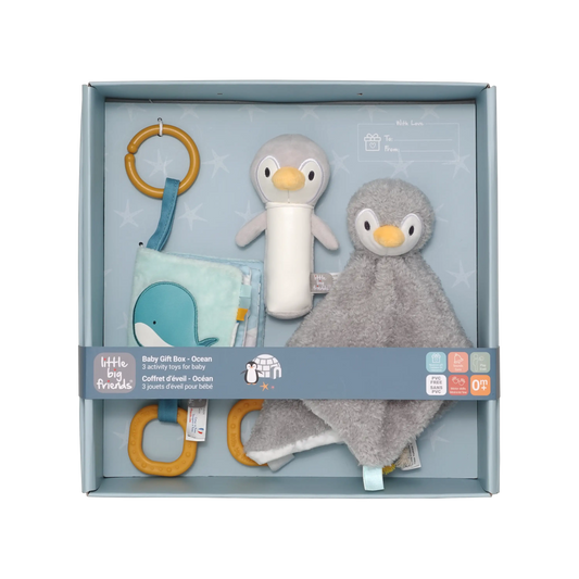 A baby gift set by Little Big Friends inside a light blue box, featuring a plush penguin toy, a grey penguin comforter, a blue whale fabric toy, and wooden ring toys.