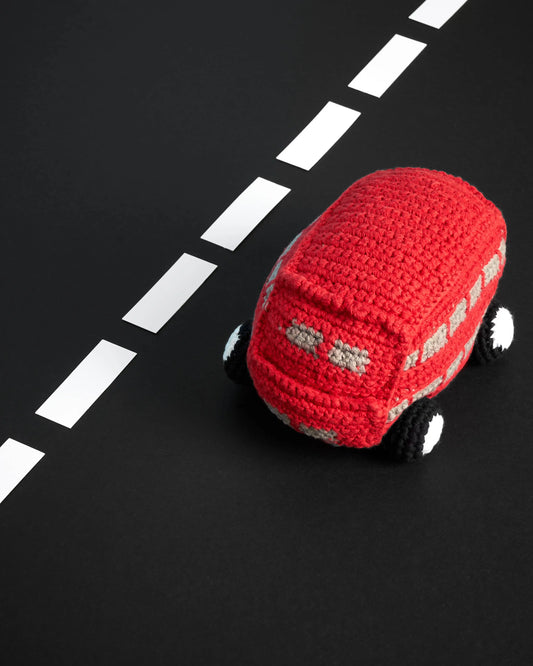 A red crocheted toy car with black and white wheels, placed on a black surface with a white dashed road line.
