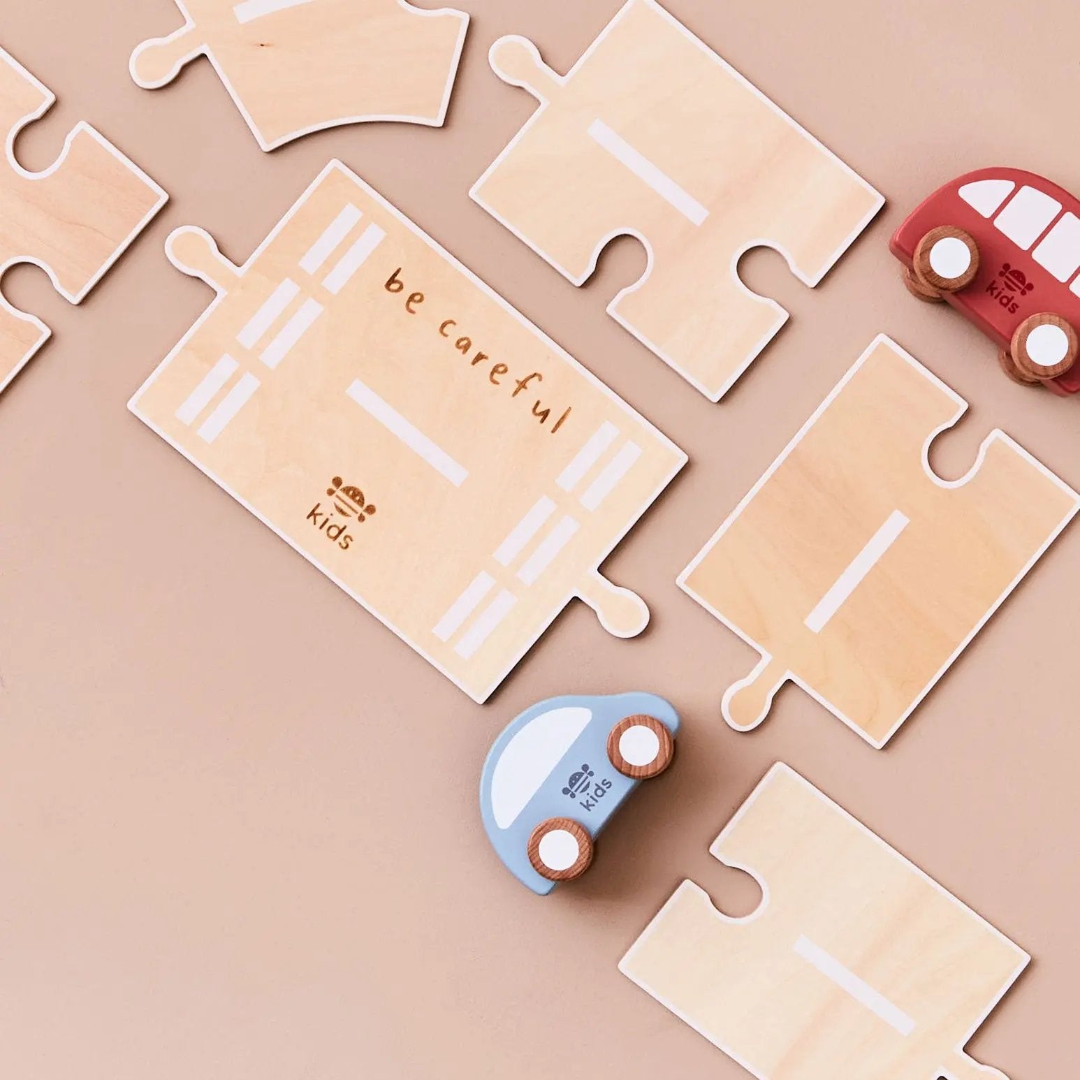 Wooden puzzle pieces with a 'be careful' message and toy cars on a beige background