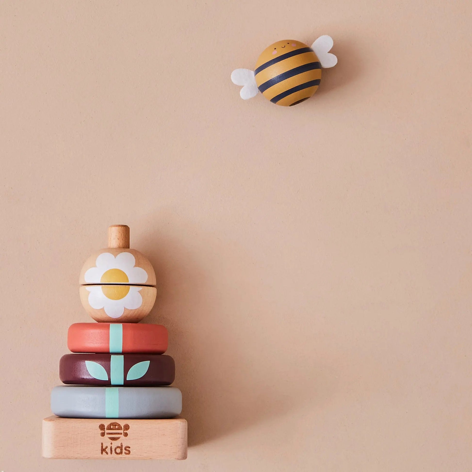 Stack of colourful wooden toys with a bee-shaped block on a beige background