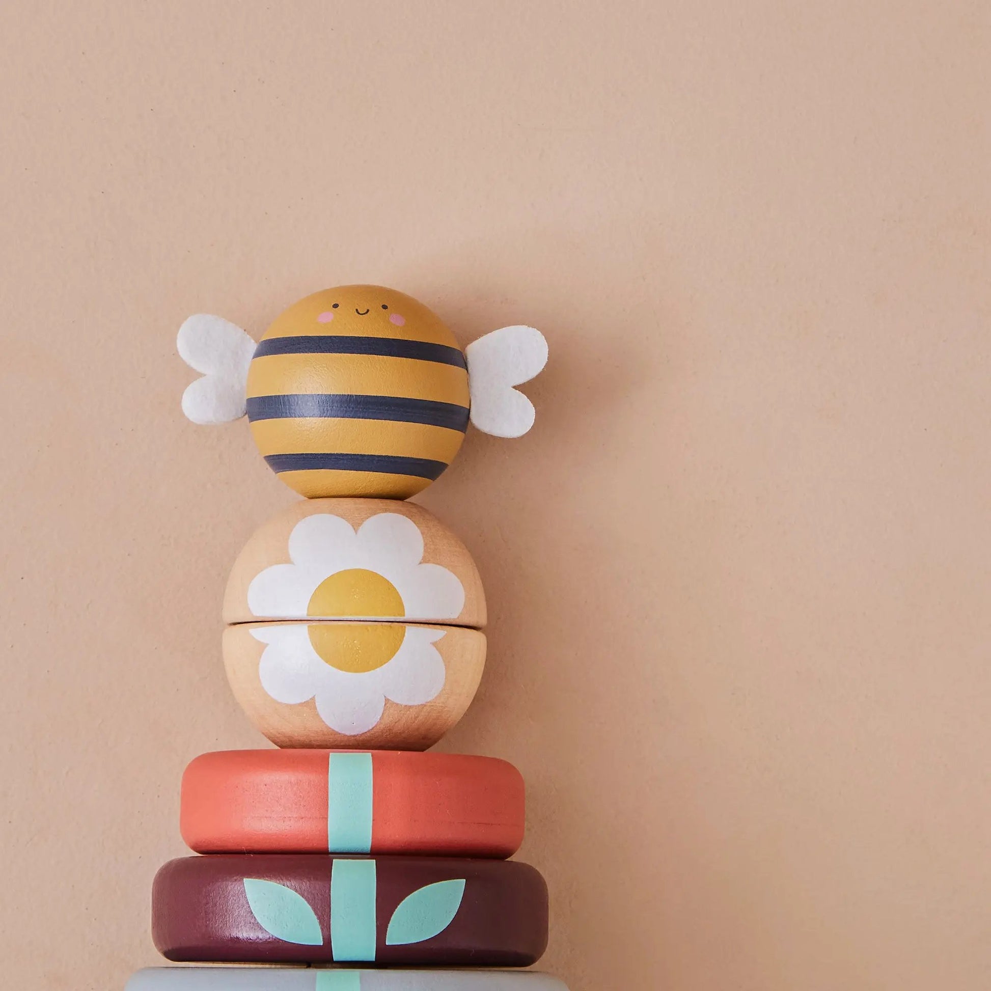 Stack of colourful wooden toys with bee and flower design on a beige background
