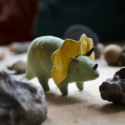 Toy triceratops dinosaur with a yellow frill on a sandy surface with rocks.