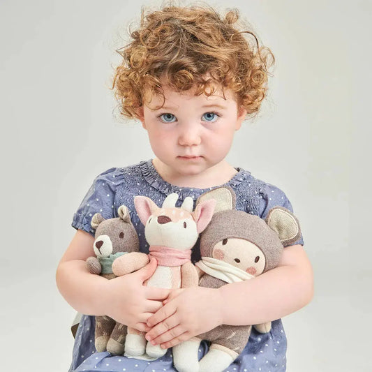 Child holding three plush toys against a plain background