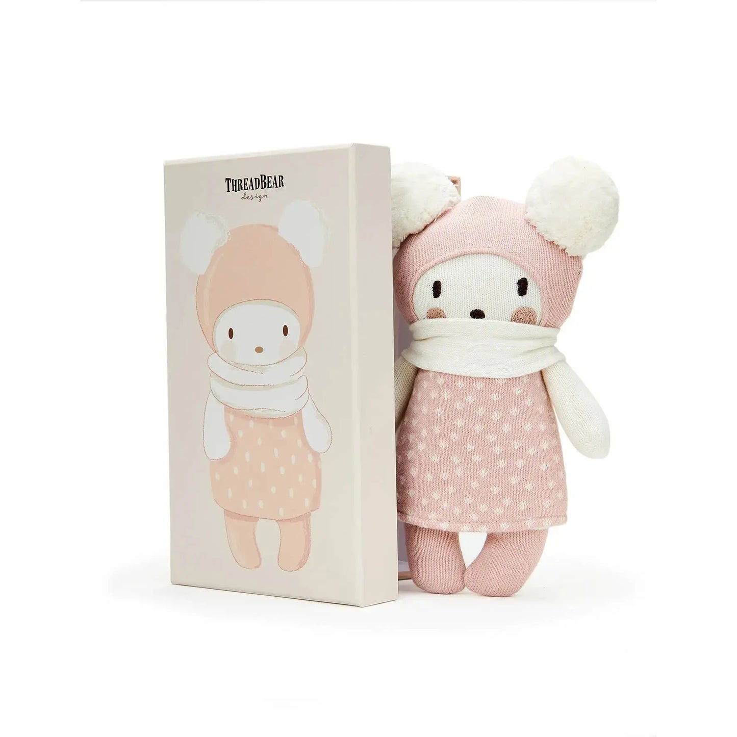 Stuffed toy with pink outfit and white hat next to its packaging on a white background
