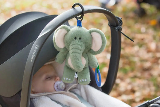 Green elephant toy hanging from a buggy handle with a blurred outdoor background