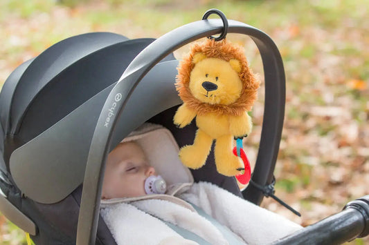Baby in a buggy with a lion toy hanging from the canopy