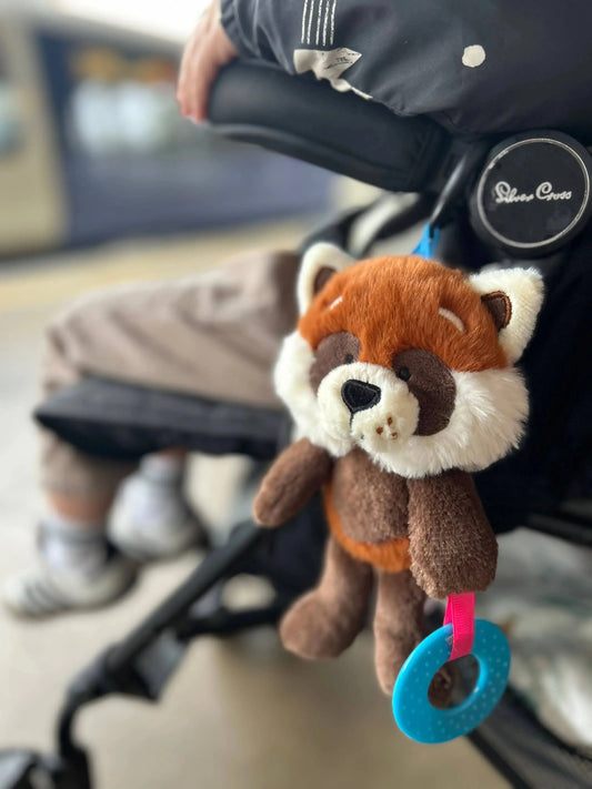 Plush red panda toy attached to a stroller with a blurred background