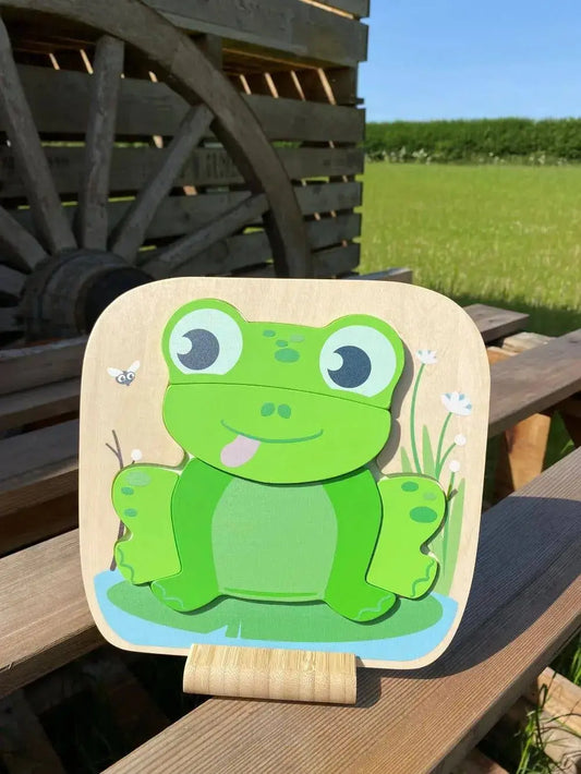 Wooden toy frog on a stand with a wooden cart and field in the background