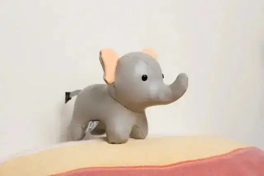 Grey elephant toy on a pink pillow against a white wall