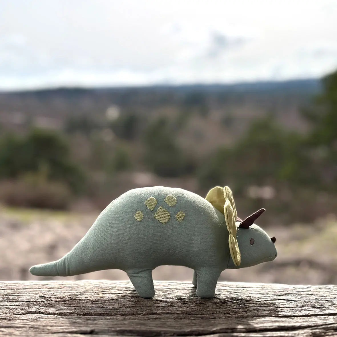 Plush dinosaur toy with a yellow hat on a wooden surface with a blurred natural background