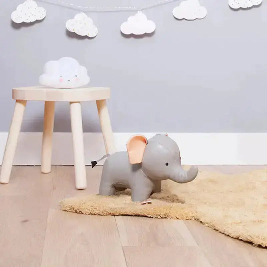 Gray elephant toy on a beige rug with a wooden stool and cloud-shaped object in a room.