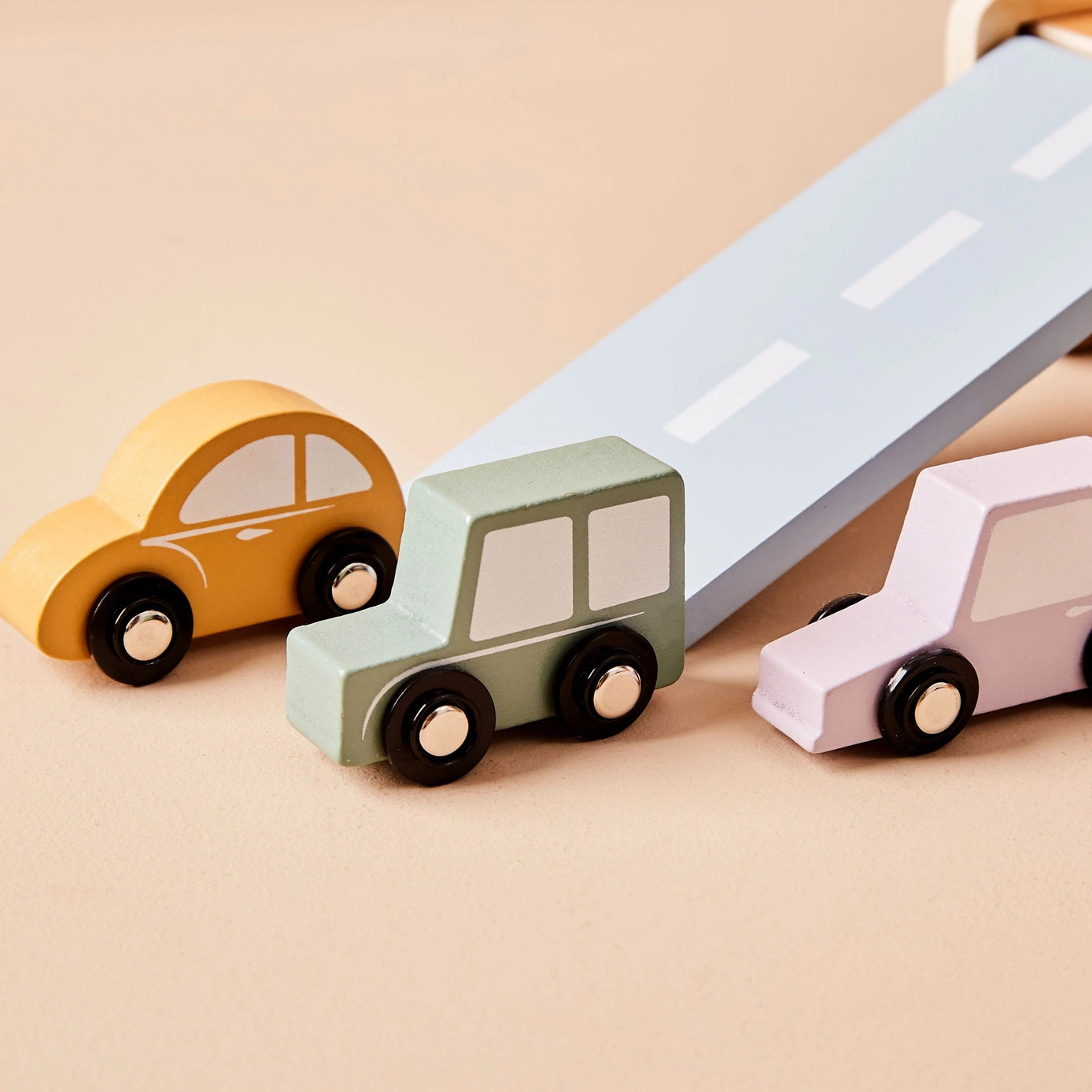 Three colourful toy cars which are part of a wooden ferry on a road with a beige background