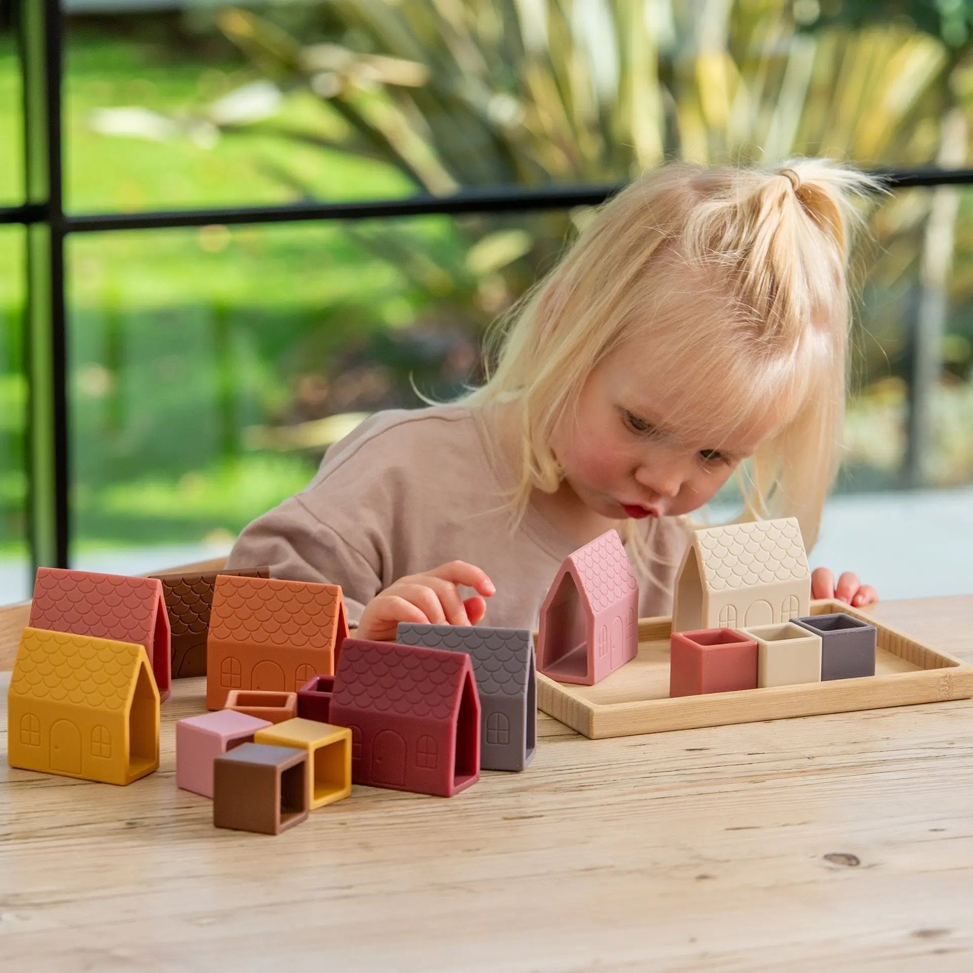 Child playing with colourful wooden blocks on a wooden table outdoors.
