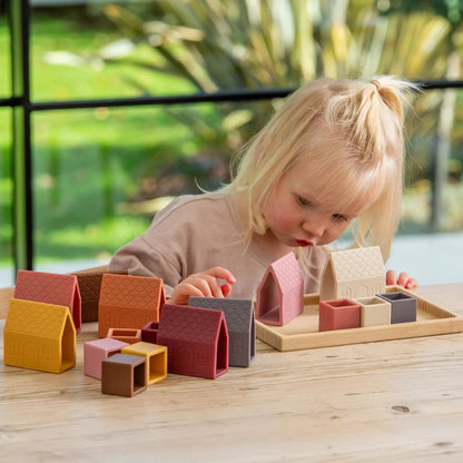 Child playing with colourful wooden blocks on a wooden table outdoors.