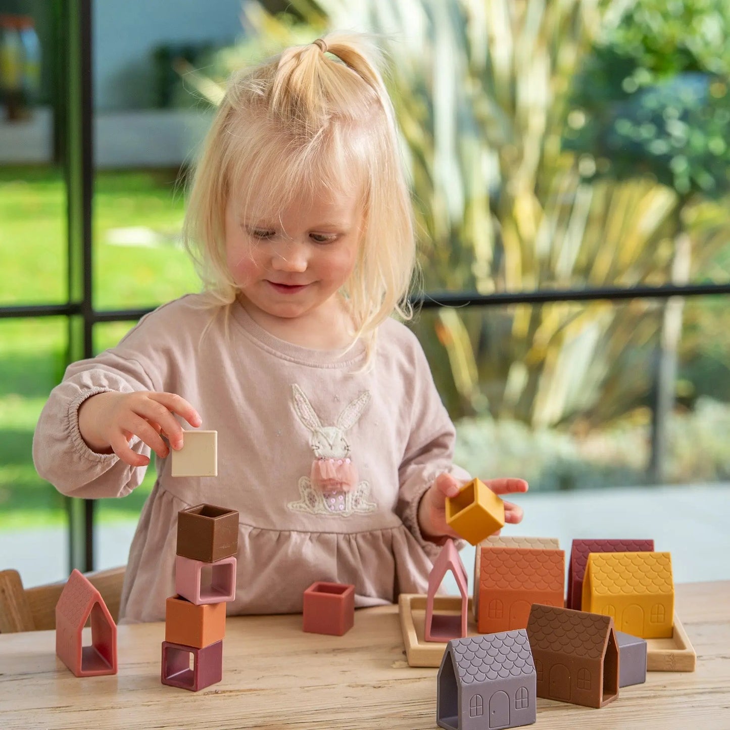 Child playing with colourful building blocks on a table outdoors.