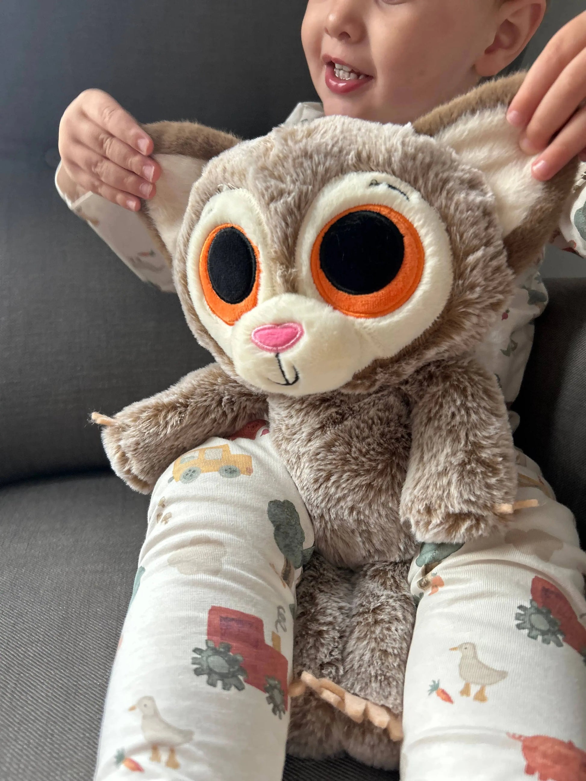 Child holding a plush toy with large eyes and a pink nose on a gray couch.