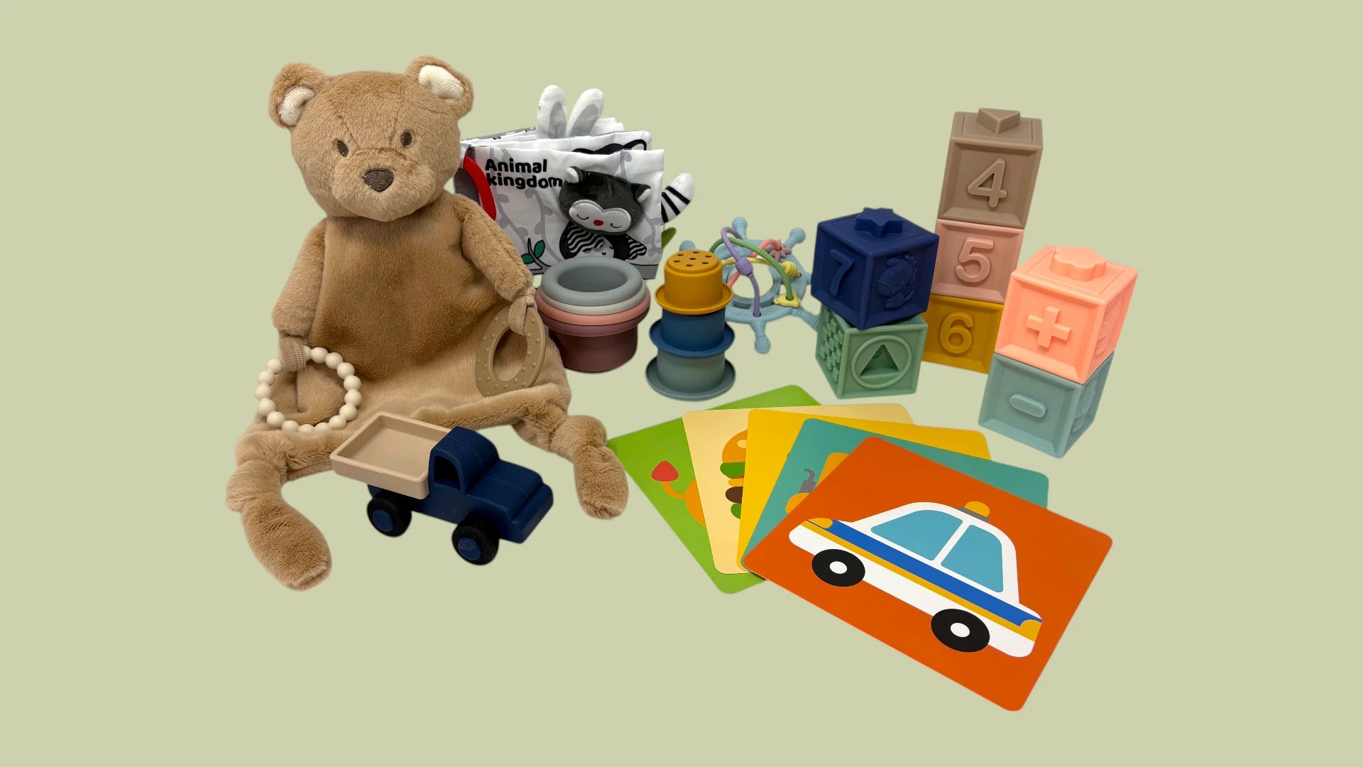 Collection of toys including a teddy bear, cars, blocks, and cards on a beige background