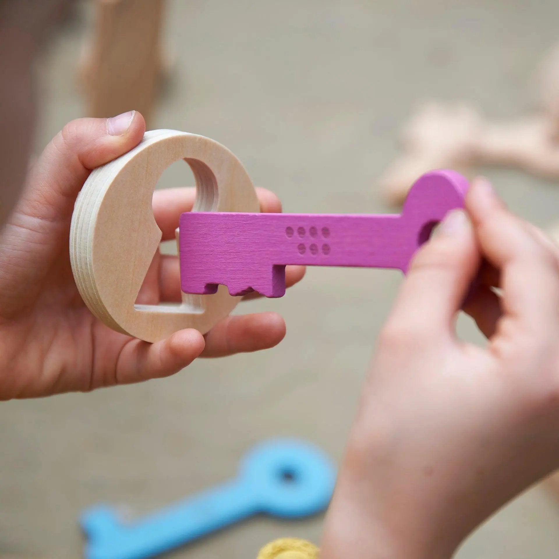 Hands holding a wooden keyhole with a purple key against a blurred background