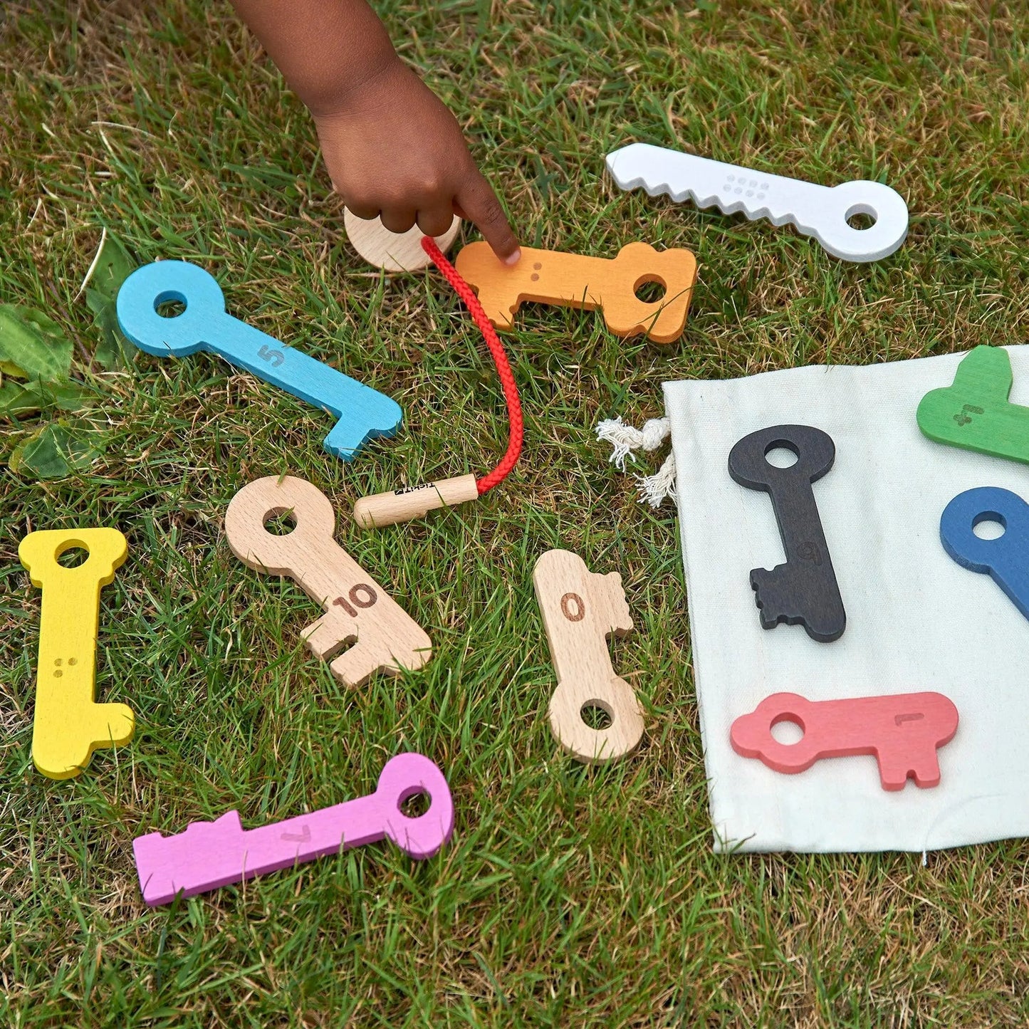 Colourful key-shaped toys on grass with a hand reaching for one of them.