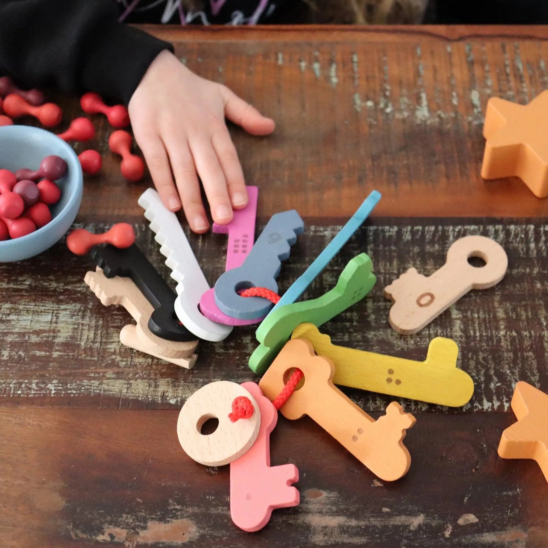 Colourful wooden keys on a wooden table with a hand reaching for one of them.