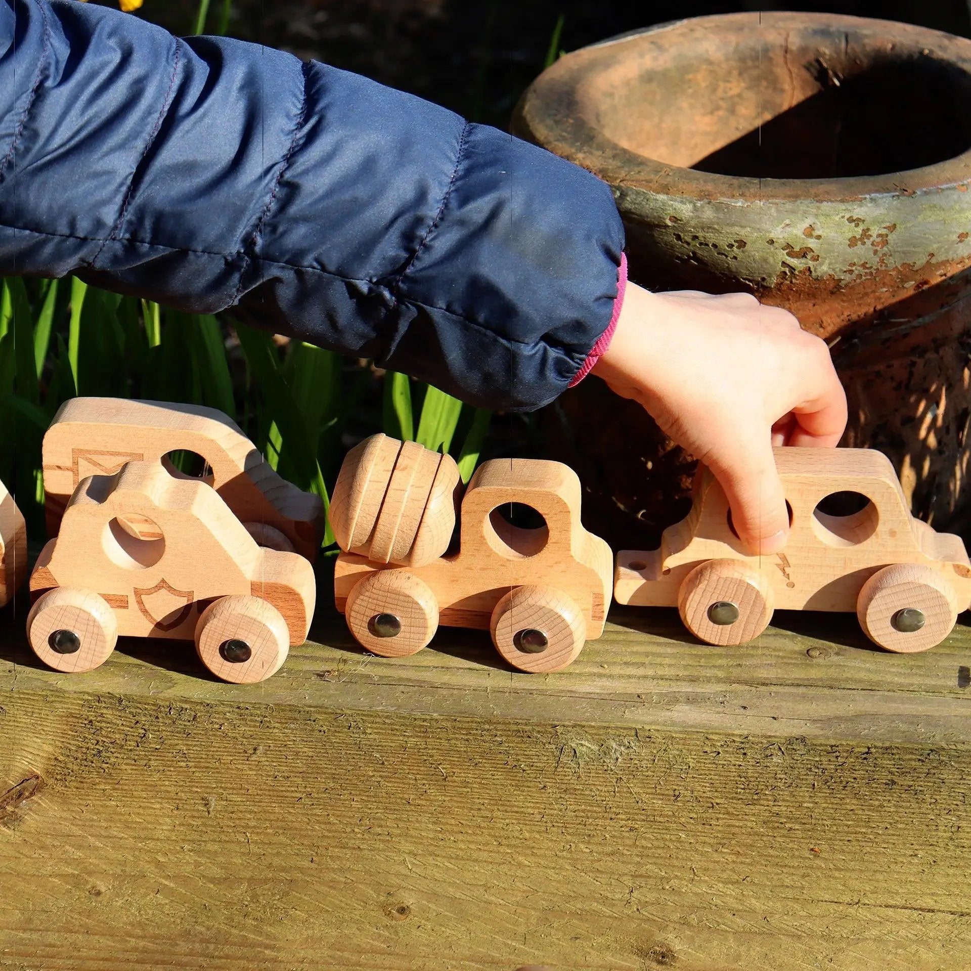 Child playing with wooden toy cars on a wooden surface outdoors.