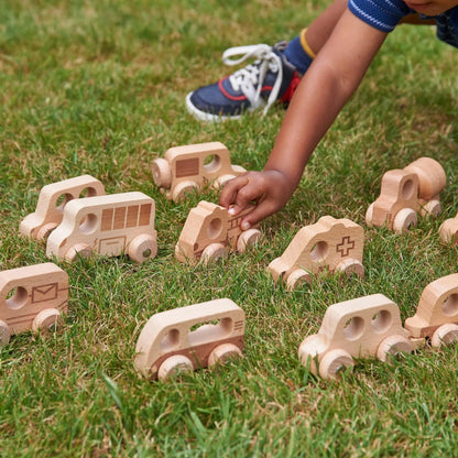 Wooden toy cars on grass with a child's hand reaching out