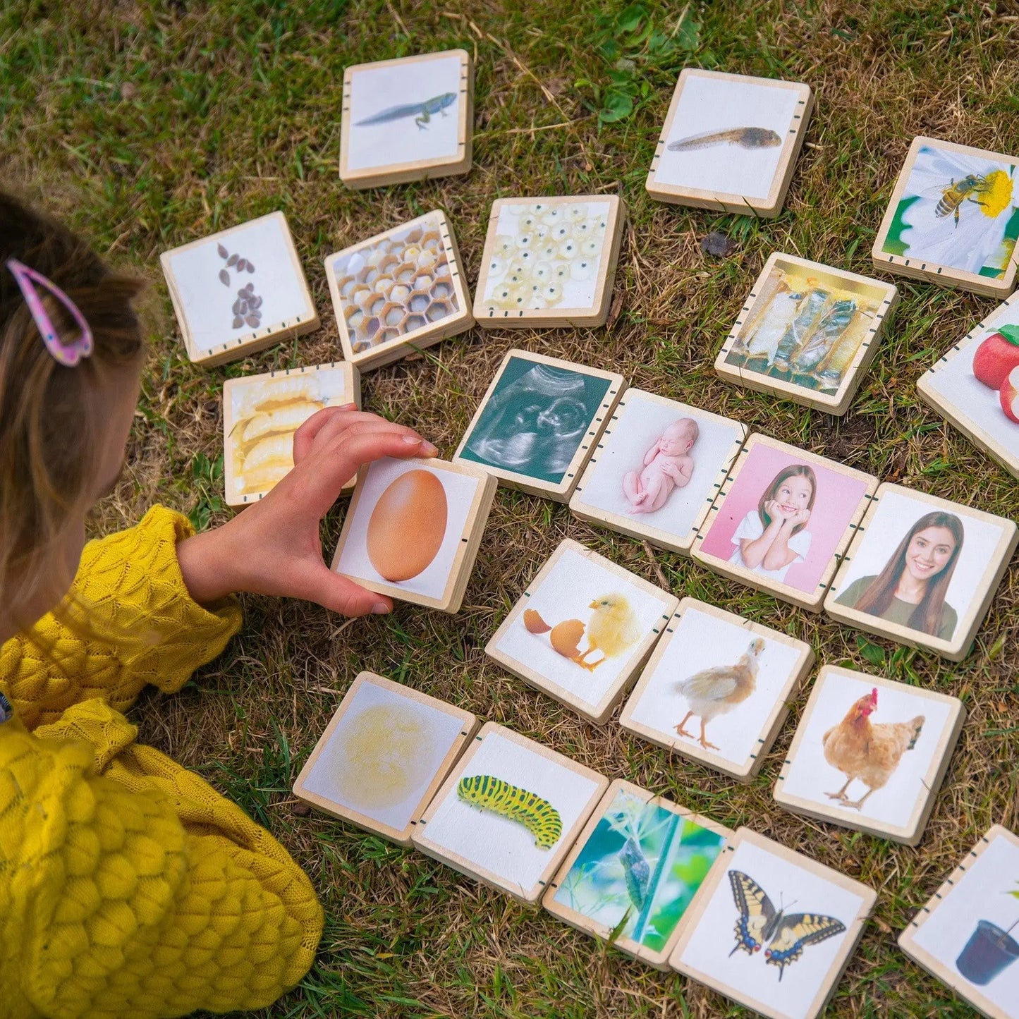 Child playing with educational tiles featuring various images on grass