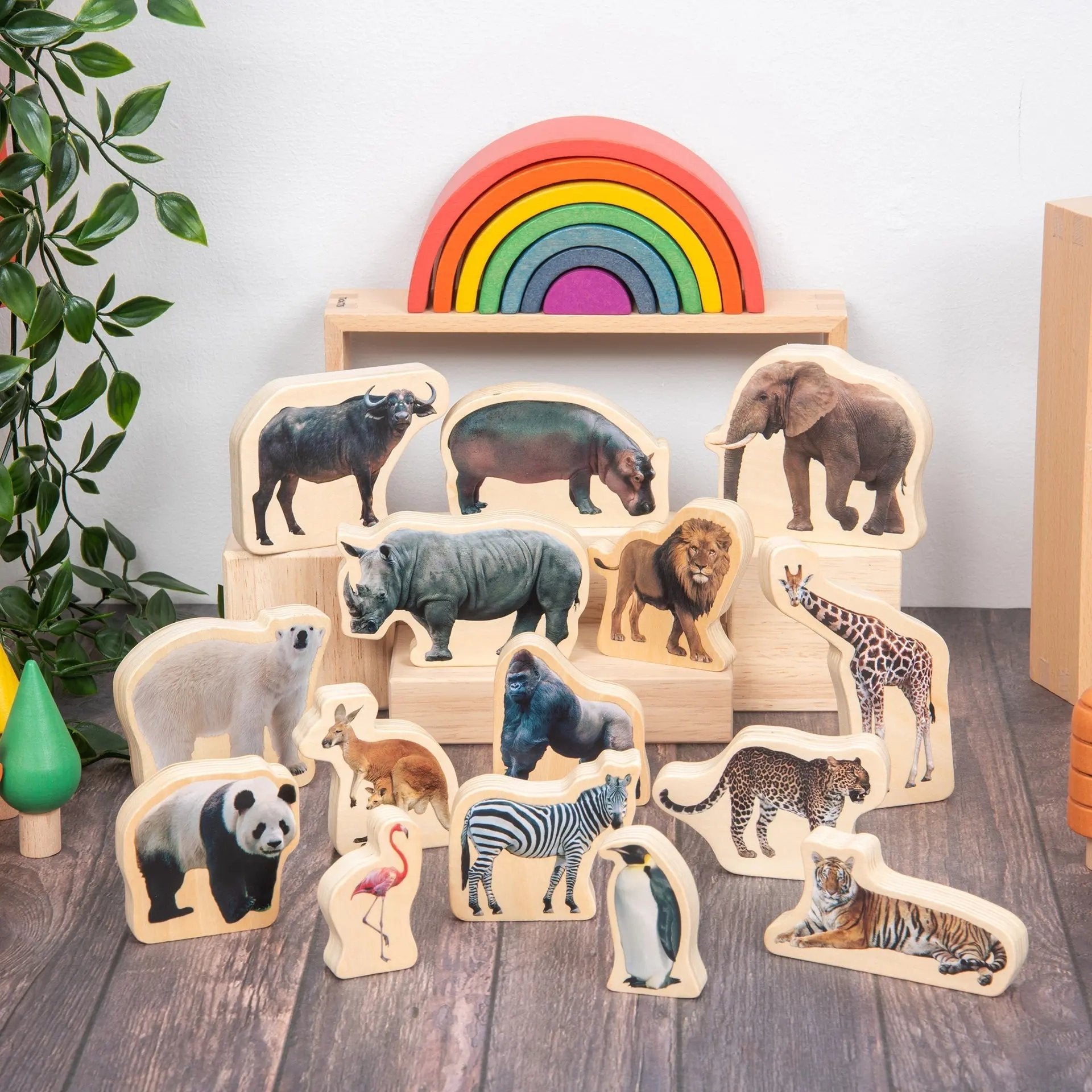 Set of wooden animal figures on a wooden floor with a rainbow toy in the background.