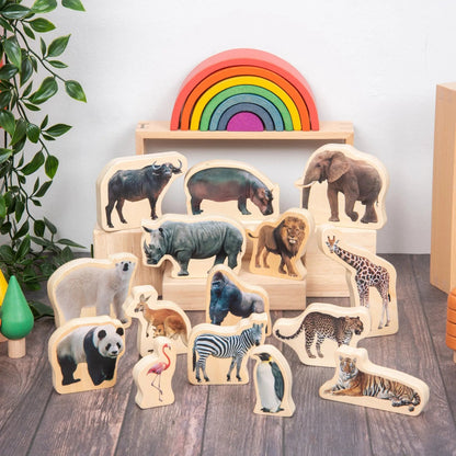 Set of wooden animal figures on a wooden floor with a rainbow toy in the background.