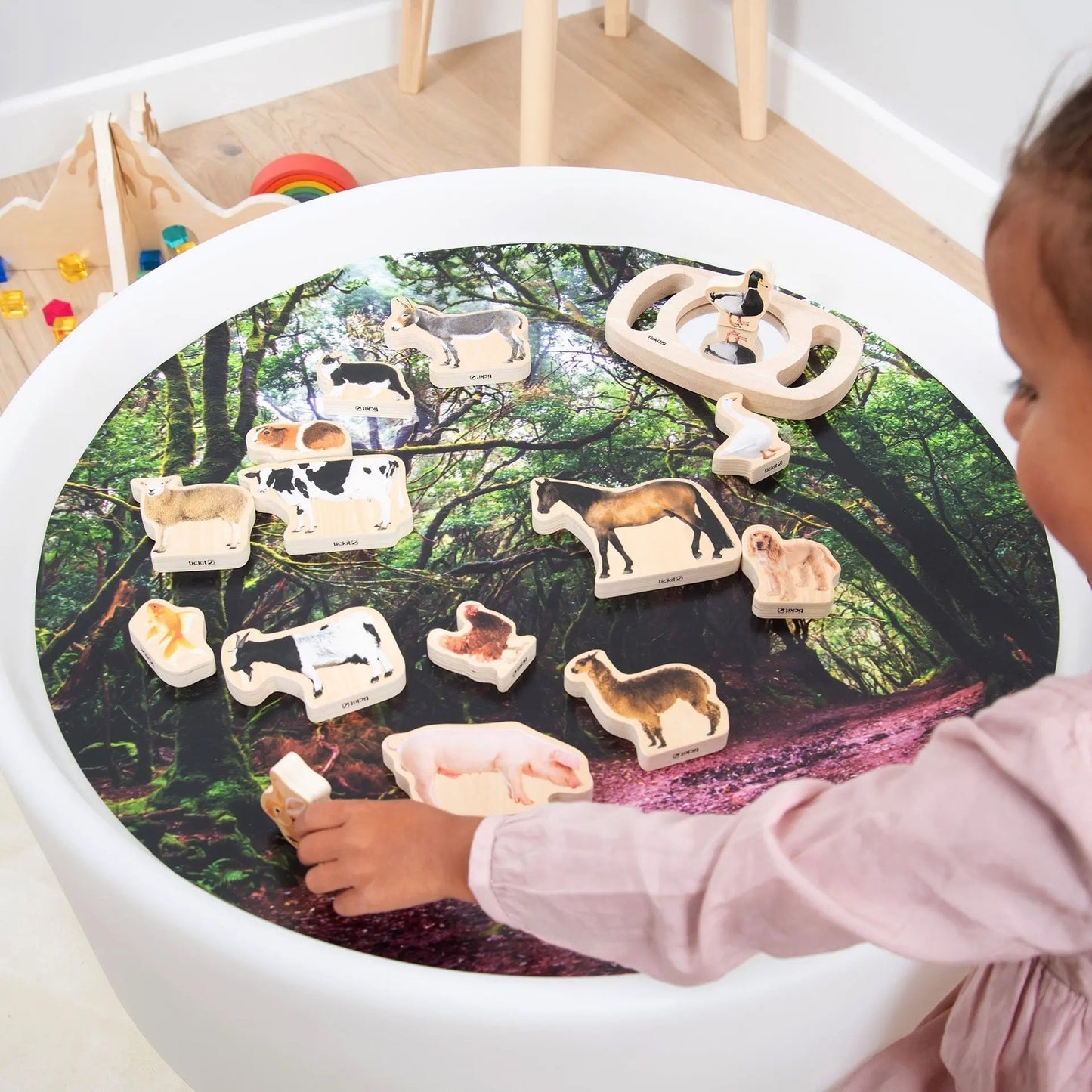 Child playing with animal figurines on a round table with a forest design