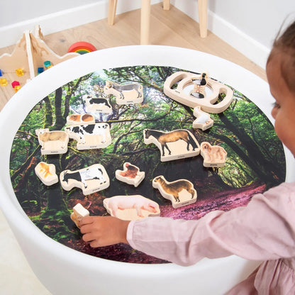 Child playing with animal figurines on a round table with a forest design